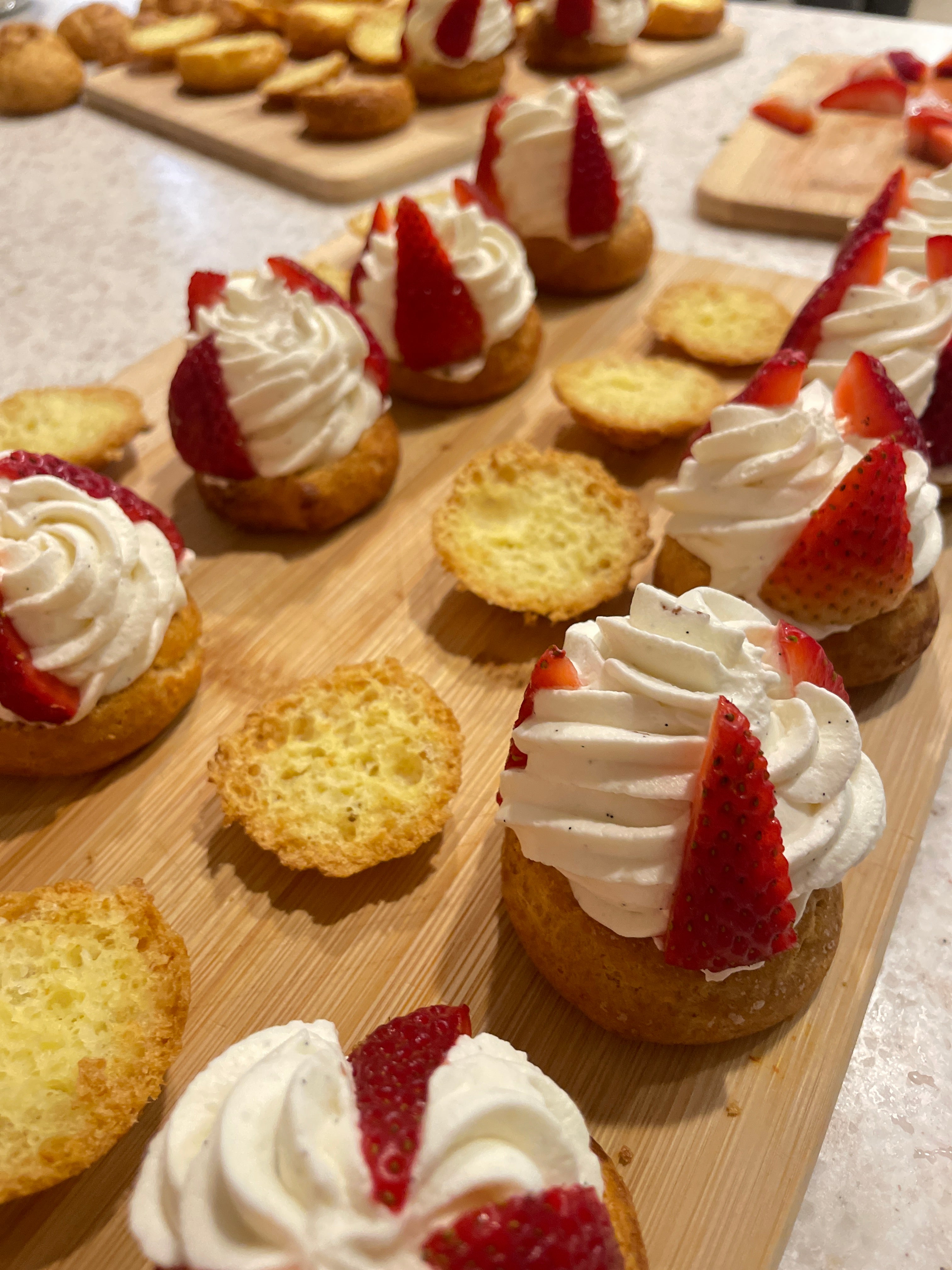 Gluten-free cream puffs filled with vanilla whipped cream and topped with fresh strawberry slices, displayed open on a wooden board before serving.
