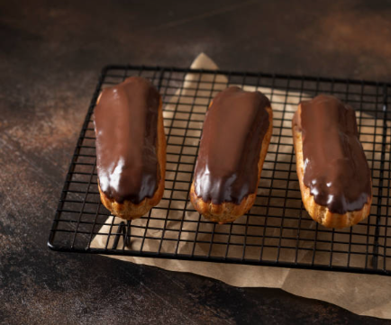 Homemade chocolate éclairs filled with pastry cream and topped with glossy chocolate fondant glaze on a parchment-lined tray.