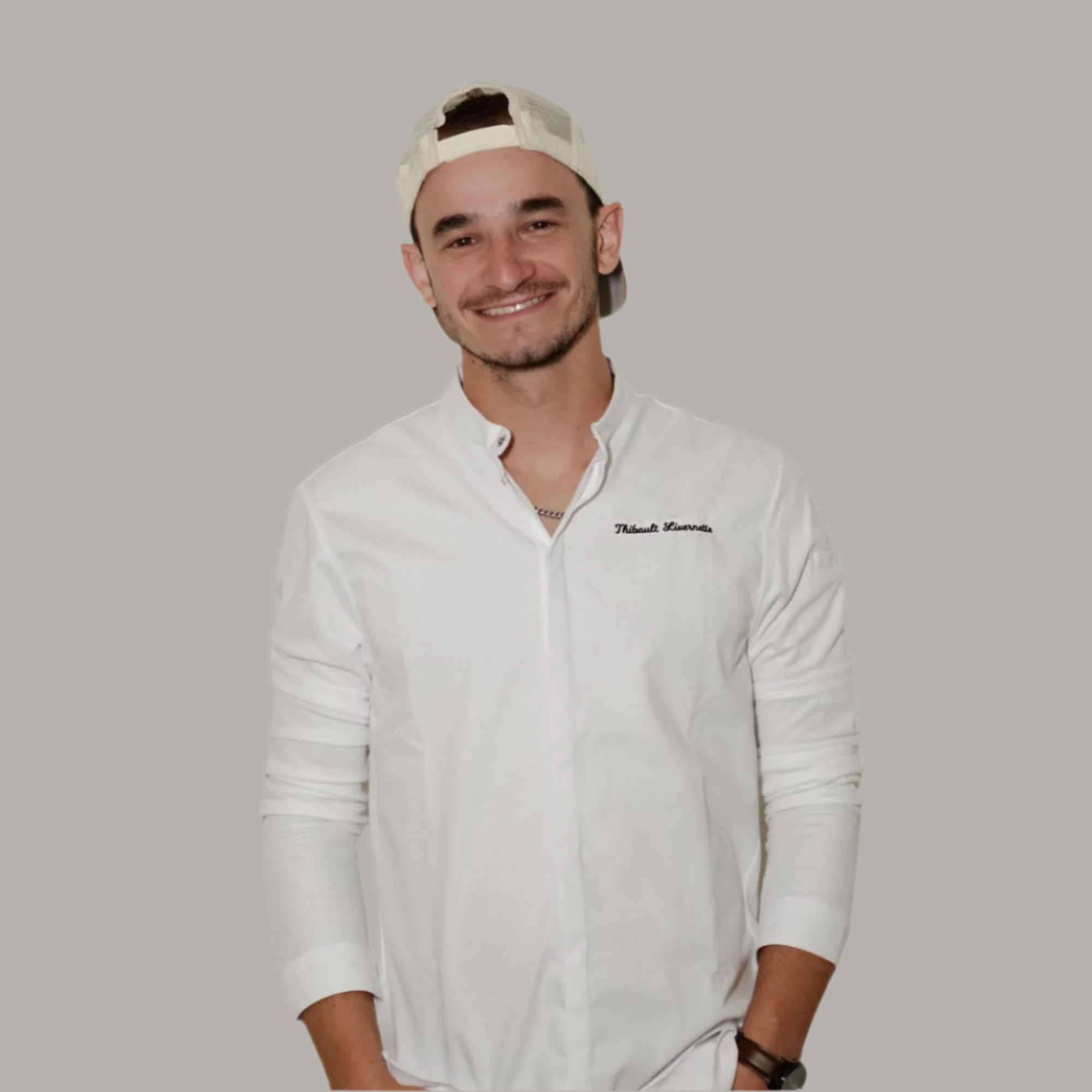 Pastry Chef wearing a white shirt with a logo and a cap against a plain background